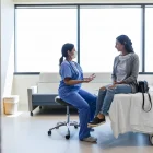 The young adult female doctor gestures while talking to the young adult female patient in the ER examination room.