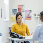 A middle aged female patient of Asian decent sits across the desk from her female doctor as they discuss her mental health concerns.