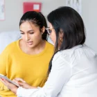 The teen looks at the tablet as her female doctor explains the exam results during the visit.