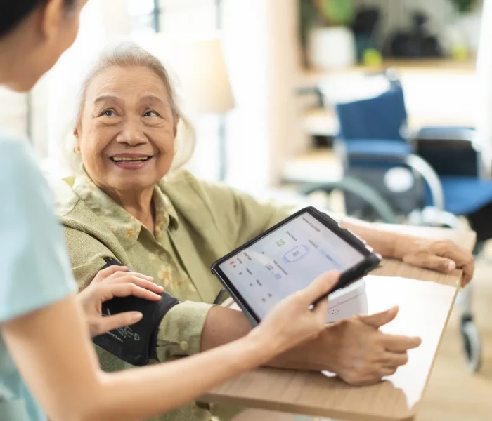 Woman asian nurse taking blood pressure of a senior woman patient at home.Home care healthcare professional using digital tablet