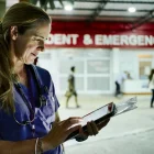 Nurse dressed in medical scrubs standing outside the hospital emergency entrance at night and using digital tablet