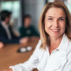 Portrait of confident, professional woman sitting at her office looking directly at the camera with a poised expression. Mature businesswoman dressed in white shirt. The setting appears to be a modern indoor space with soft natural lighting. Senior businesswoman at modern office contributing to a calm, professional atmosphere.