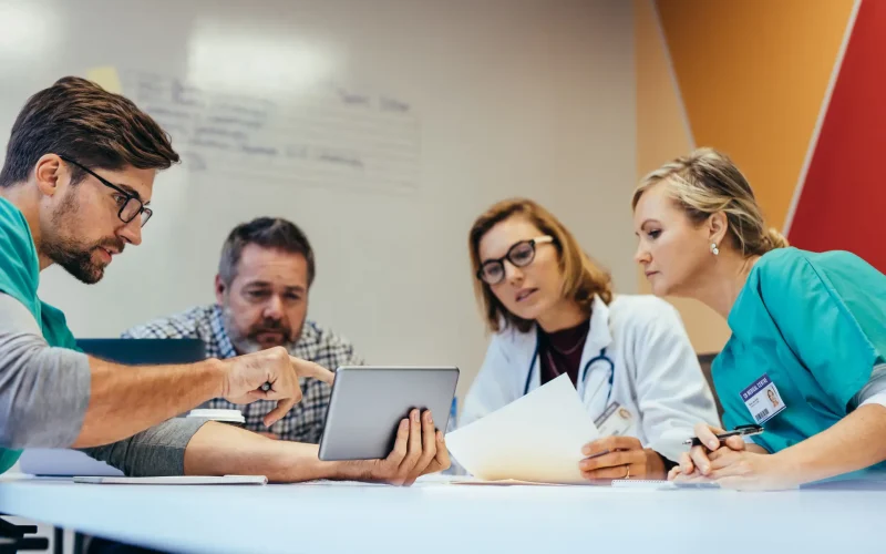 Team of healthcare workers having a meeting in boardroom. Medical professional briefing medication plan to colleagues on digital tablet.