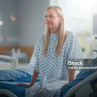 Modern Hospital Ward: Beautiful Caucasian Female Patient Resting on a Bed, Fully Recovering after Successful Surgery, Sickness or Coronavirus she Smiles. Behind Her Window with a Beautiful Sunny View